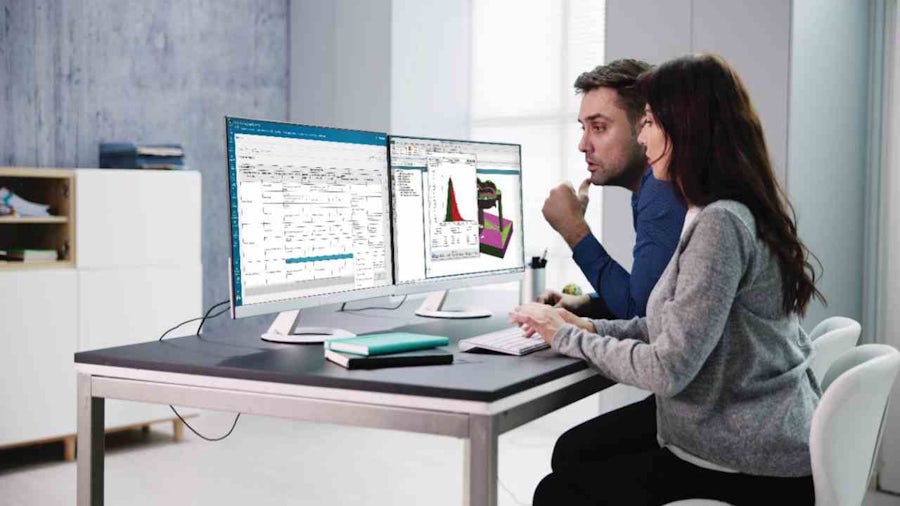 Zwei Ingenieure, die an einem Schreibtisch zusammenarbeiten und Fahrzeugsimulationsdaten auf zwei Monitoren analysieren.