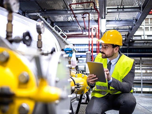 A man in a hard hat inspects factory floor machinery