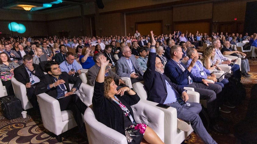 Attendees at Realize LIVE Americas in a crowd holding up their hands to answer a poll from the speaker on stage.