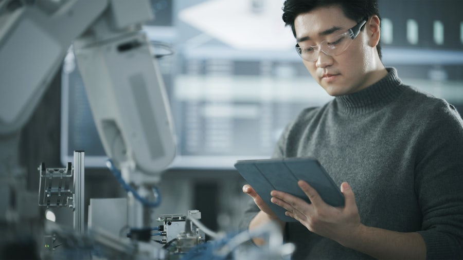 A scientist wearing protective eyewear is looking at a tablet in a lab. 