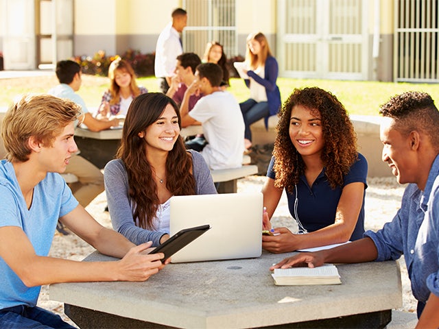 Eine Gruppe von Studenten um einen Tisch herum, die sich unterhalten und lächeln.