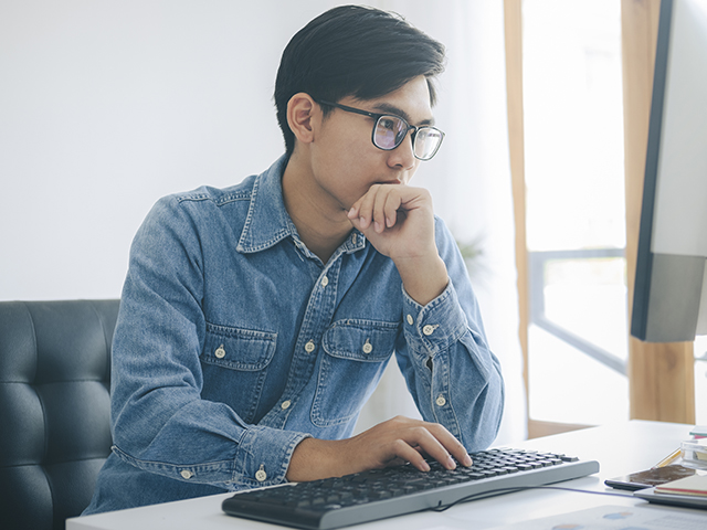 A man is sitting at a desk looking at his computer. 