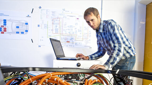 A man with a laptop is looking at wiring. 