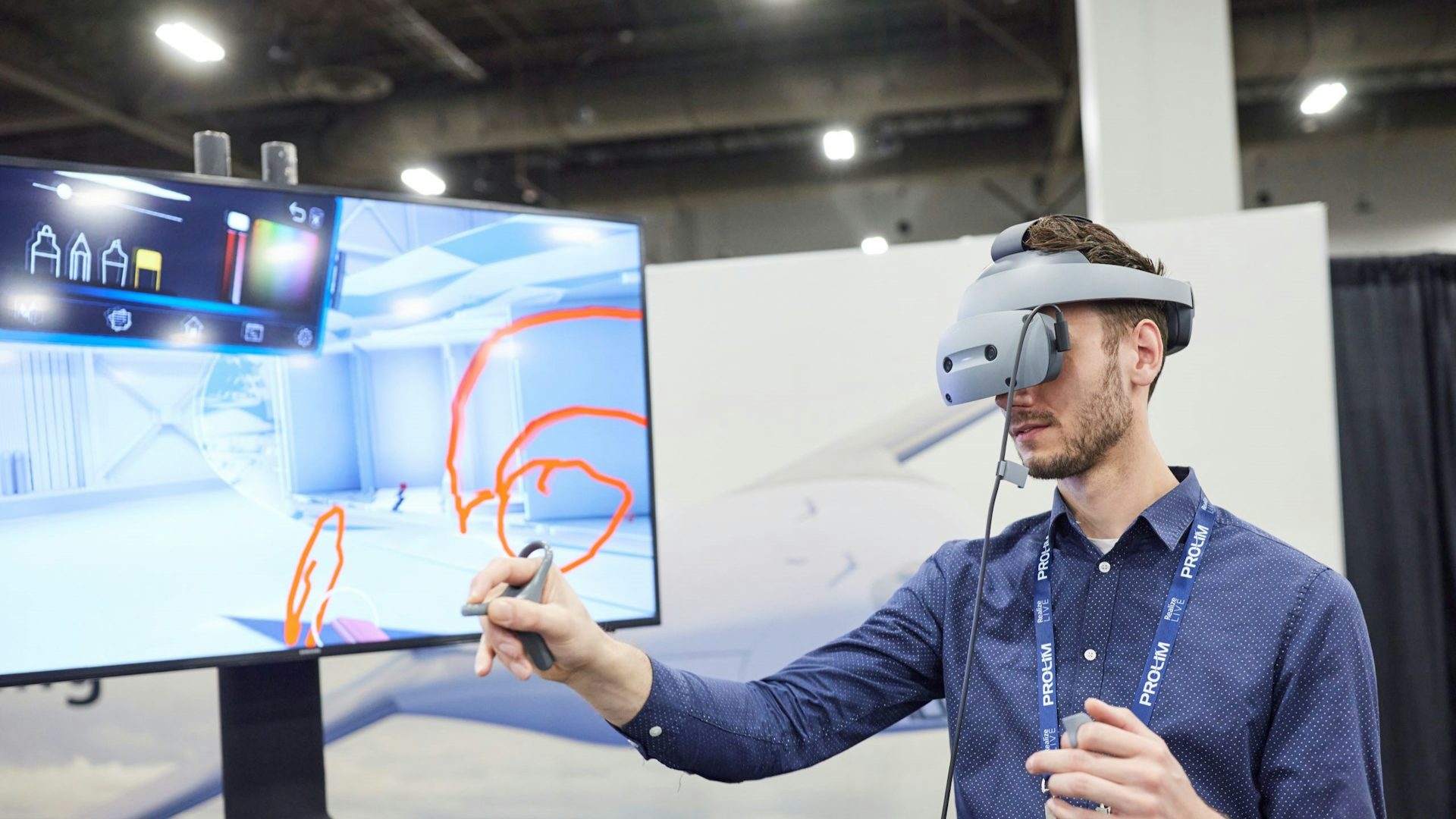 At a Siemens Realize LIVE conference, a man working with a virtual reality (VR) headset and controller, works in a simulated manufacturing facility.