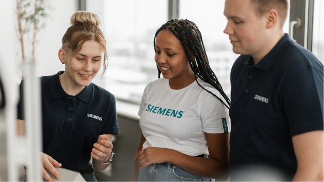 Three people wearing Siemens t-shirts looking at a card.