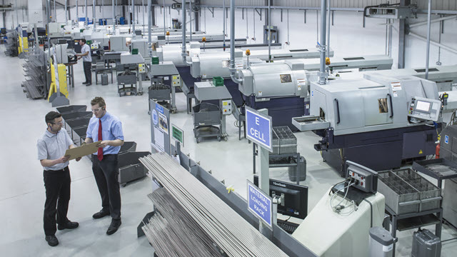 Two men wearing safety glasses and suits are looking at a tablet in a factory.