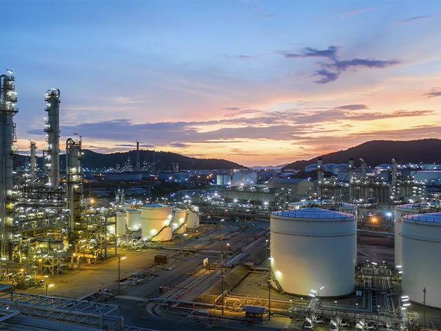 Industrial manufacturing plant at night with smokestacks emitting steam, reflected in a canal or river.