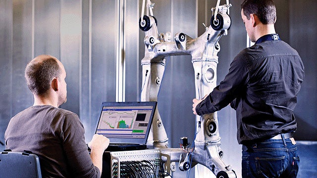 Dos hombres trabajando en una pieza de la máquina. Una persona utiliza el software de simulación y pruebas de Simcenter en un portátil mientras otra inspecciona la pieza.