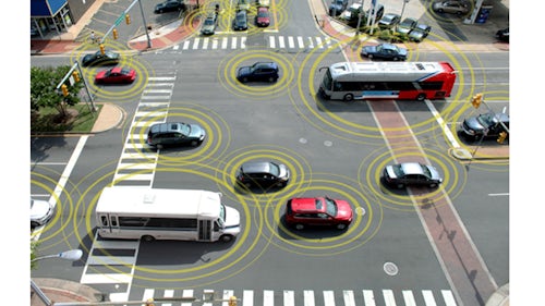 Photo of road intersection with multiple vehicles passing through. Yellow concentric circles around each vehicle represent wireless communications.