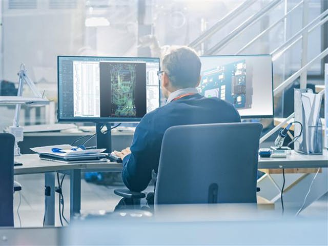 An engineer works with designs on two computer monitors.