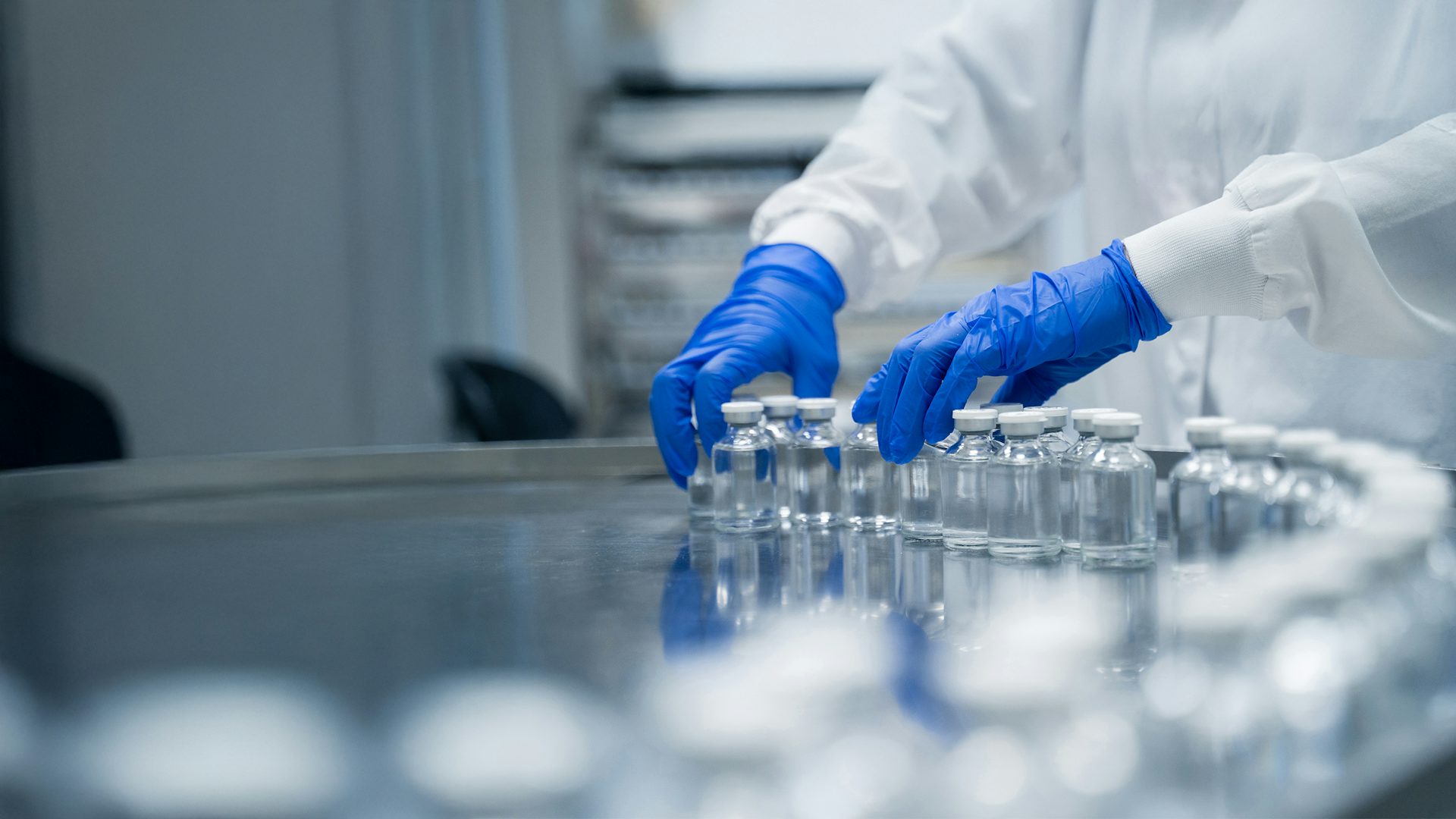 Close-up of hands working in a pharmaceutical factory, handling sterile bottles.