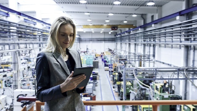 A woman reviewing a manufacturing process plan on a tablet inside a factory.