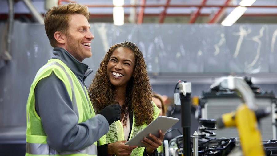 Two manufacturers on the shop floor look at a tablet and discuss the production line.