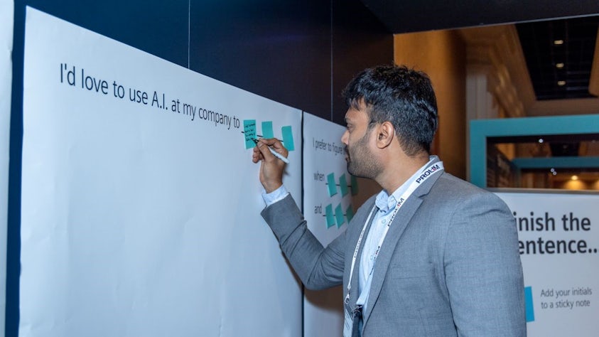 Man writing on a sticky note on a board about how companies are using AI. Part of the Innovation Hub research projects from Realize LIVE 2023. 
