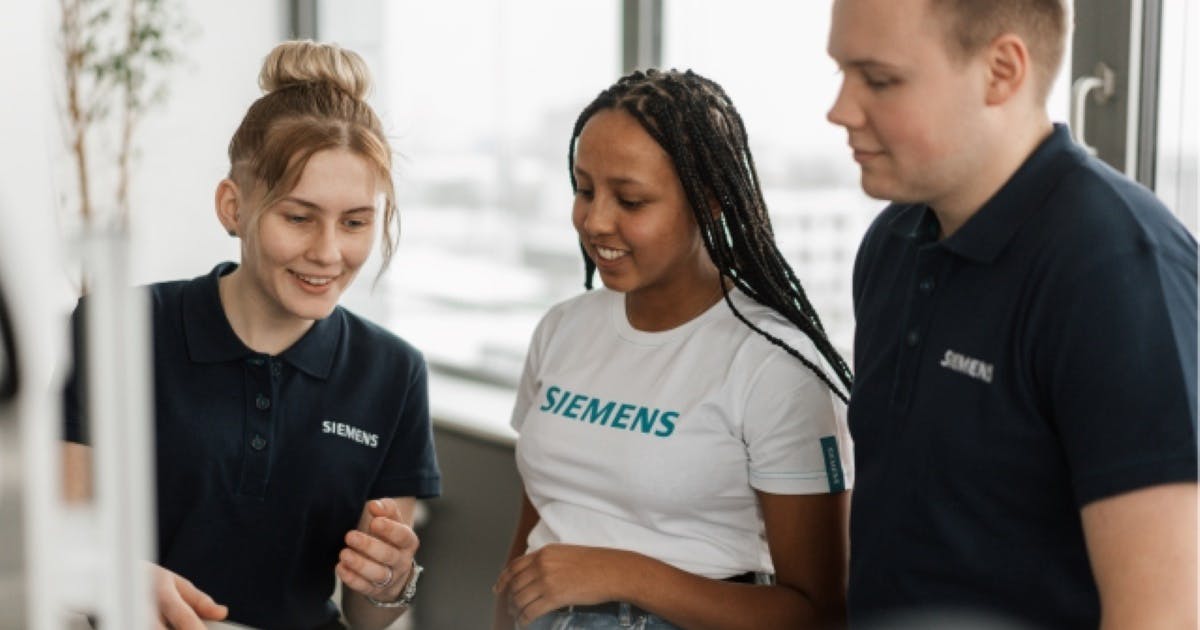 Three students wearing Siemens T-shirt having a discussion at an event.