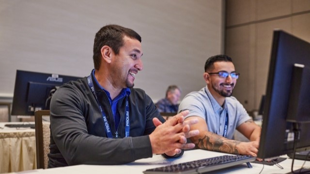 Two men sit at a computer and share a desktop screen.