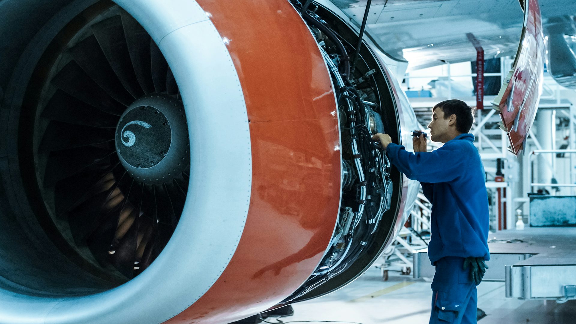 A mechanic in blue working on one of the engines of an airplane. 
