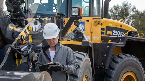 An engineer in the field testing heavy equipment with Simcenter rugged data acquisition hardware connected to testing software on a mobile device.