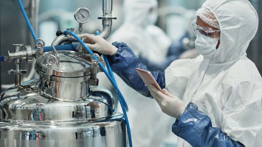 A person in a lab coat and mask operates a machine in a laboratory setting.