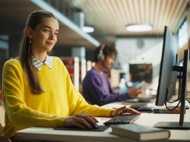 Zwei Studenten sitzen an einem Schreibtisch und schauen auf einen Monitor