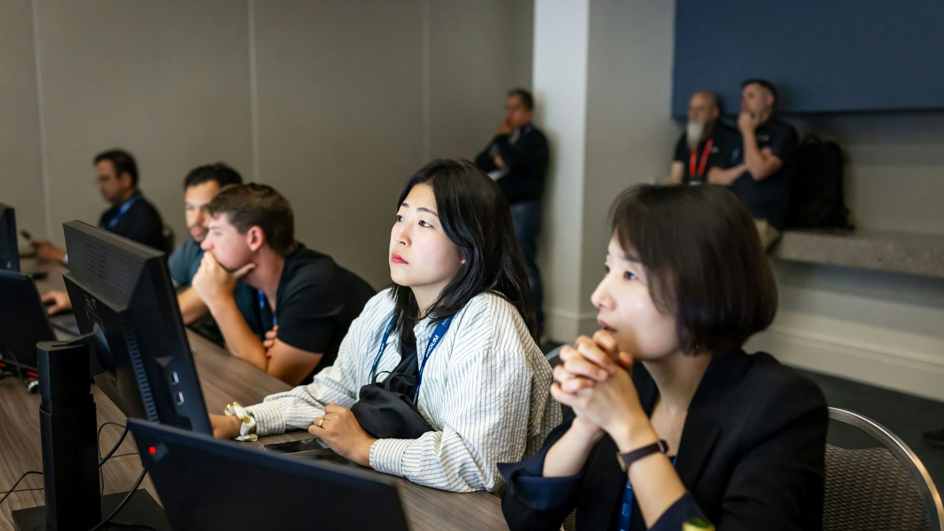 Professional attendees engaged in interactive technology session at corporate conference, featuring diverse participants using laptops and digital devices in modern meeting space.
