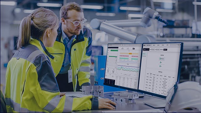 Male and female engineer working on a desktop computer in a factory.