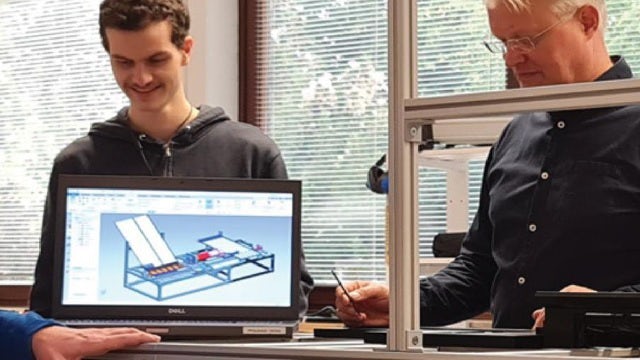 Two engineers working on a new design while a third views NX CAD on a computer monitor.