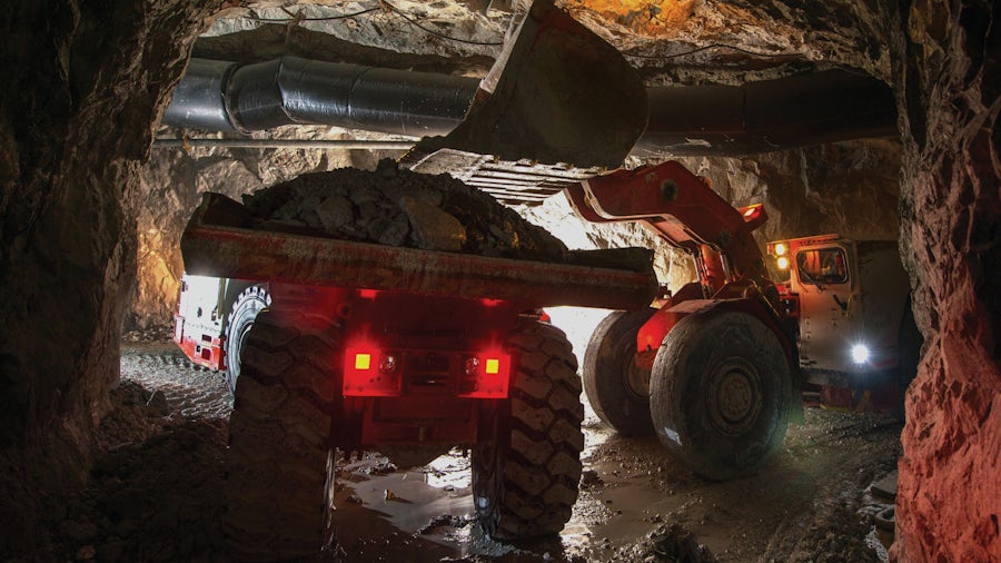 A dump truck full of ore driving from a mine into the sunlight. 