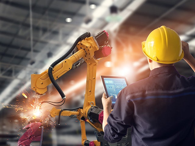 Ein Fabrikarbeiter nutzt ein Tablet, um die Leistungsfähigkeit einer Software-as-a-Service (SaaS)-Anwendung zu nutzen, um einen Roboterarm zu bedienen.
