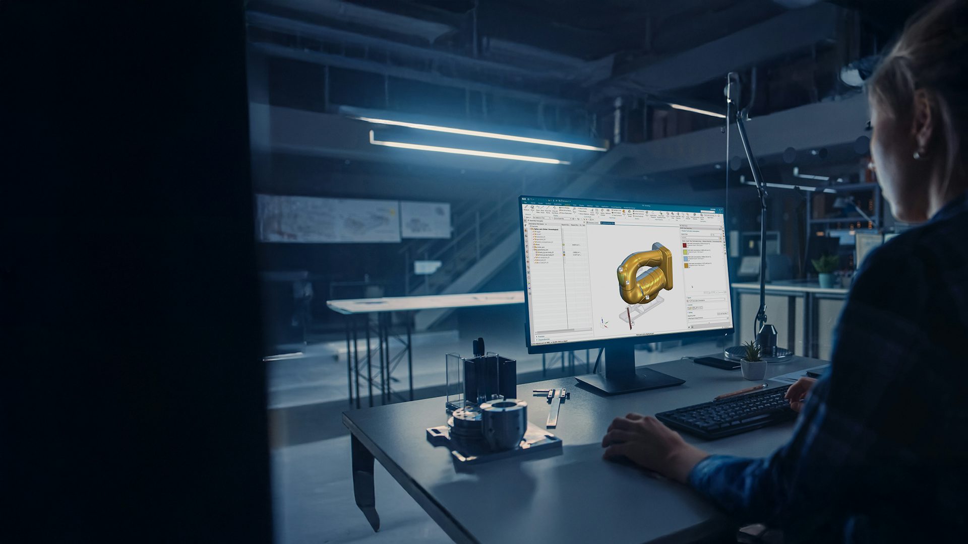 Engineer working on a desktop computer with Siemens' NX CAD modeling software displayed on the screen. She is designing a jigsaw arm and she has HD3D Visual Reporting open with sustainability calculations of her material selections.