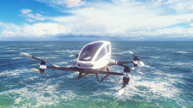 An eVTOL aircraft flies over the ocean with blue skies and white clouds in the background