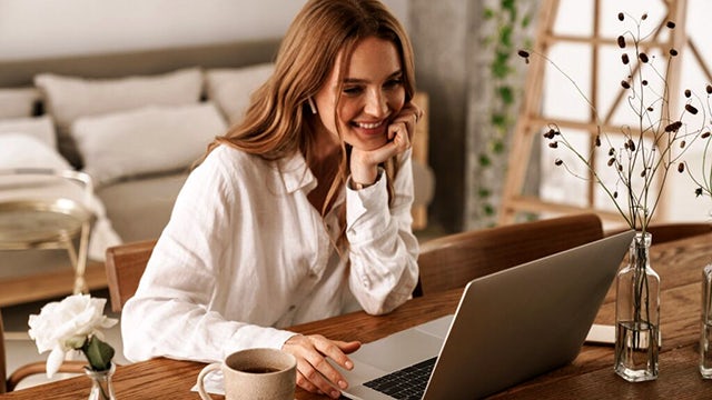 Une femme qui sourit devant son écran d'ordinateur.