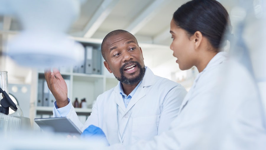 Two doctors sitting in a lab chatting while one is holding a tablet