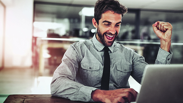 Un homme applaudit avec émotion devant son ordinateur portable et lève le poing en signe de célébration.