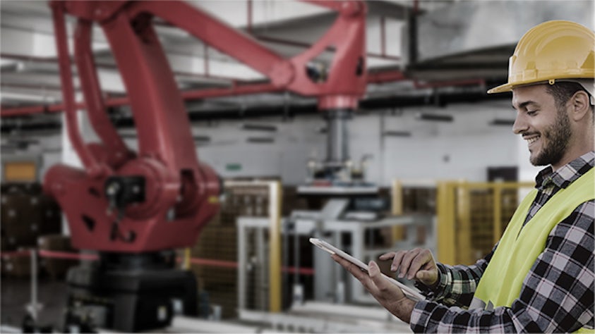 Un hombre con un casco en una fábrica mira una tablet y sonríe.