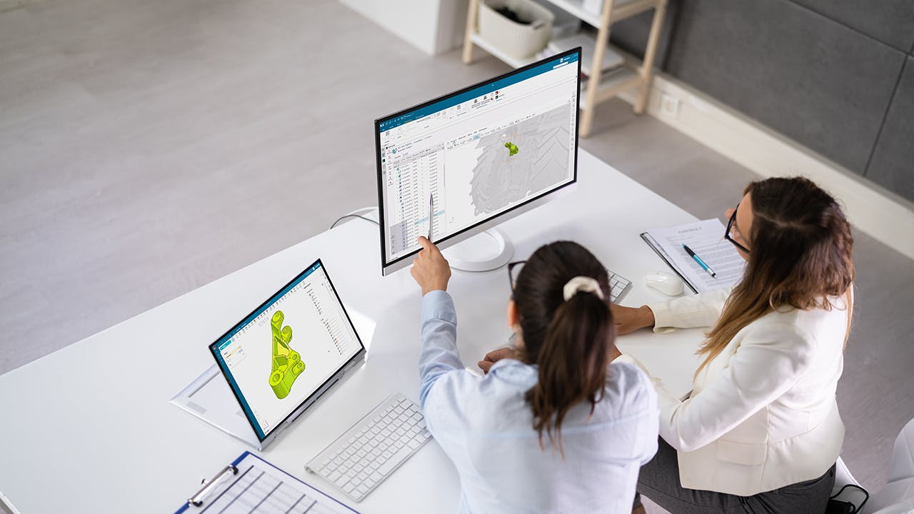 two women collaborating and viewing the same computer screen while having a laptop open with another view of the model
