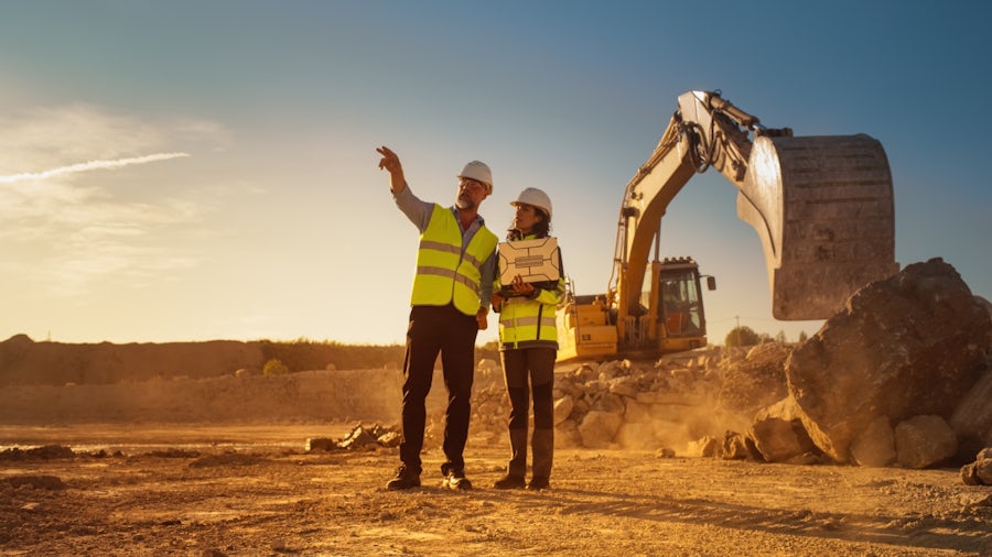 Mining engineers reviewing operations at a quarry site with heavy equipment using connected, sustainable mining practices.