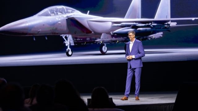 Speaker standing on stage with a backdrop of an airplane.