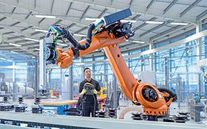 Ingenieur blickt auf einen großen orangefarbenen Roboterarm.