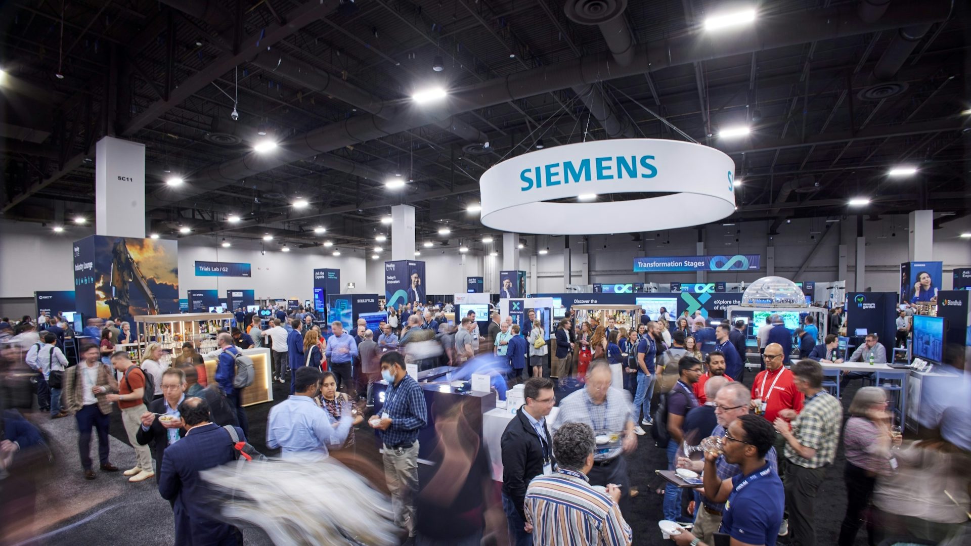 People walking the floor, visiting booths and networking under a large Siemens sign at the Realize LIVE digital transformation conference.