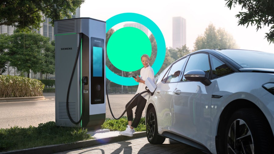 A woman is charging her electric car at a charging station, connecting the cable to the vehicle.