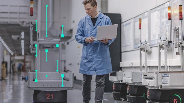 Man holding a laptop and walking the factory floor with a robot.