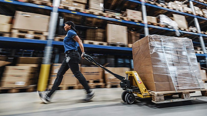 A worker pushing a pallet truck in a warehouse.