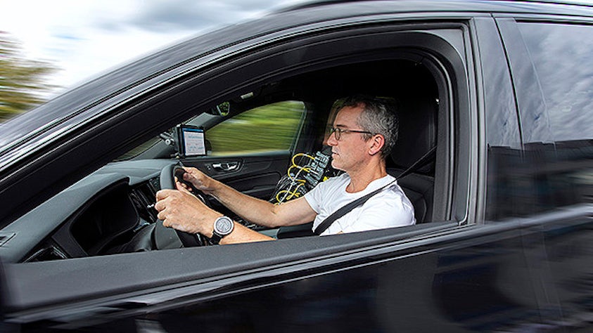 Uomo alla guida di un'auto, con le apparecchiature di test Simcenter sul sedile del passeggero che raccolgono i dati sul carico stradale
