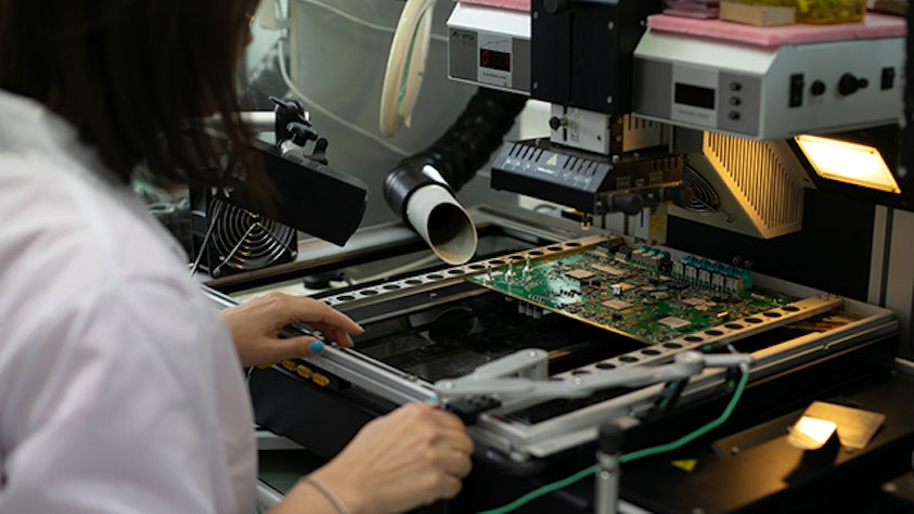 Pracownik fabryki elektroniki pracujący przy płycie elektronicznej.