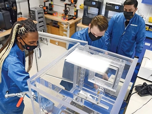 Students wearing personal protective equipment and using a manufacturing tool.