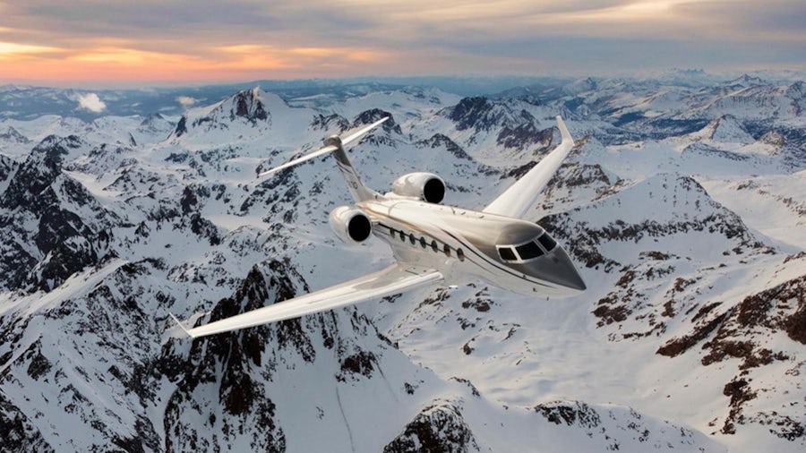 A plane is seen flying over snow mountains as the sun sets in the background. 