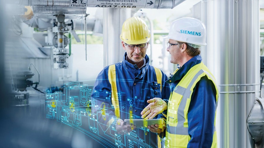 Two men work inside processing plant wearing high-visibility vests, safety glasses and hard hats.