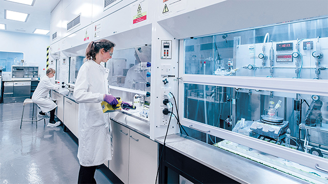 Technicians interacting with pharmaceuticals using equipment in a laboratory.