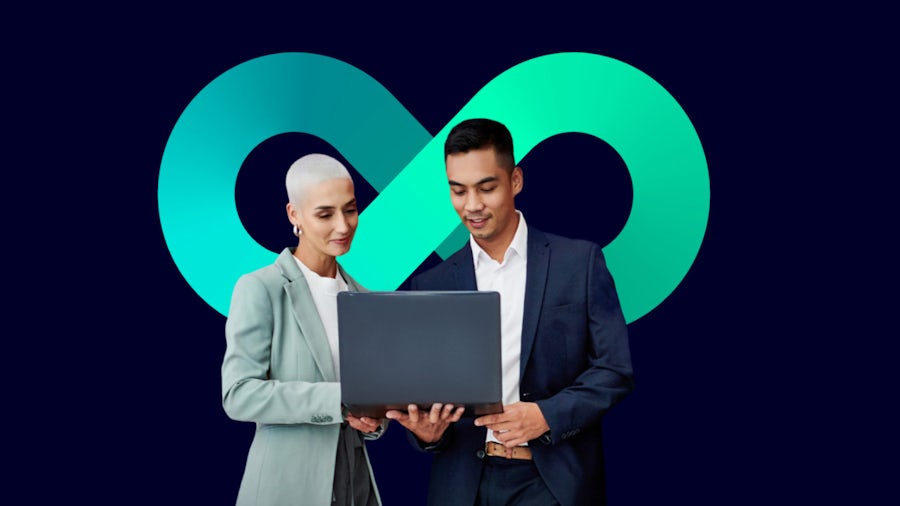  Two professionals in business suits hold a laptop while standing in front of an infinity symbol.